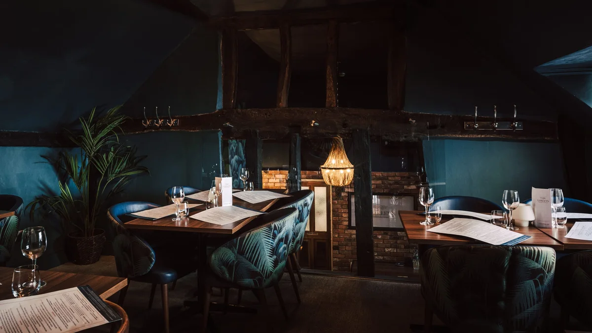 Loxleys dining room, exposed beams, chandelier and palm-print chairs in warm low light.